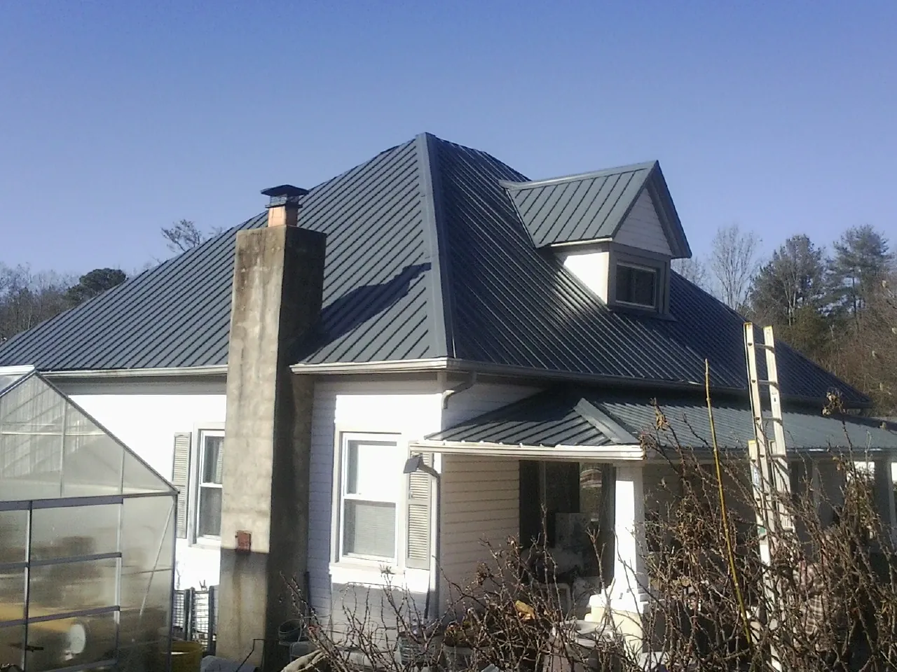 Dark blue standing seam metal roof on a white farmhouse with dormer — Slate & Tile Roof Repair by Roofing Brothers in Willow Creek