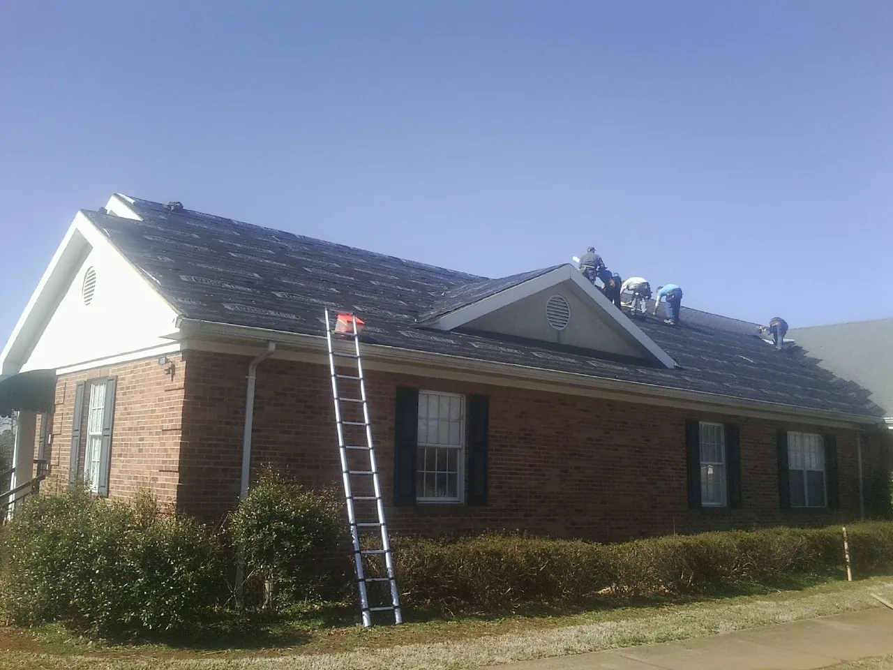 Crew tearing shingles off a brick ranch roof with a ladder set — Emergency Roof Repair work by our crew in Willow Creek