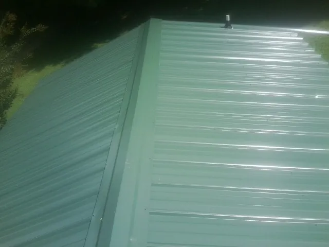 New green metal panels meeting at the ridge of a roof — Flat Roof Repair work by our crew in Willow Creek