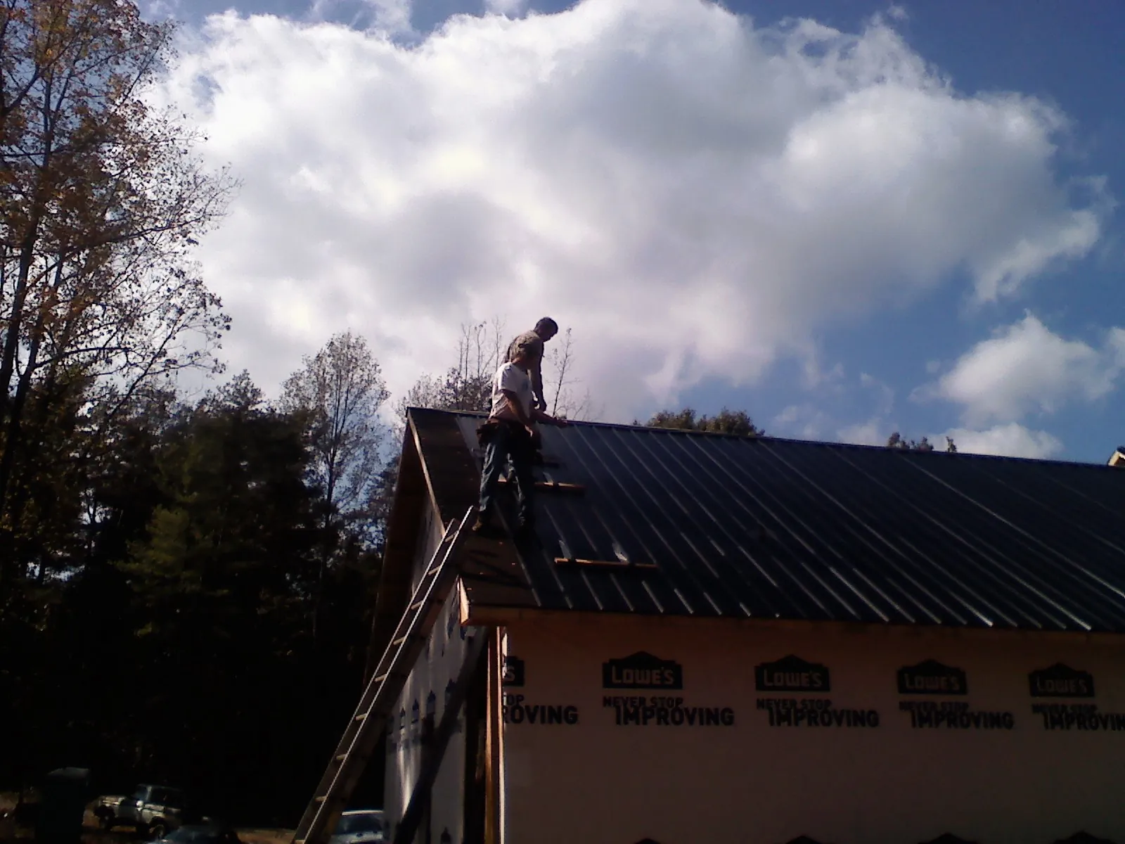 Roofer fastening dark metal panels high against a cloudy sky, from a Roof Inspection job in Willow Creek