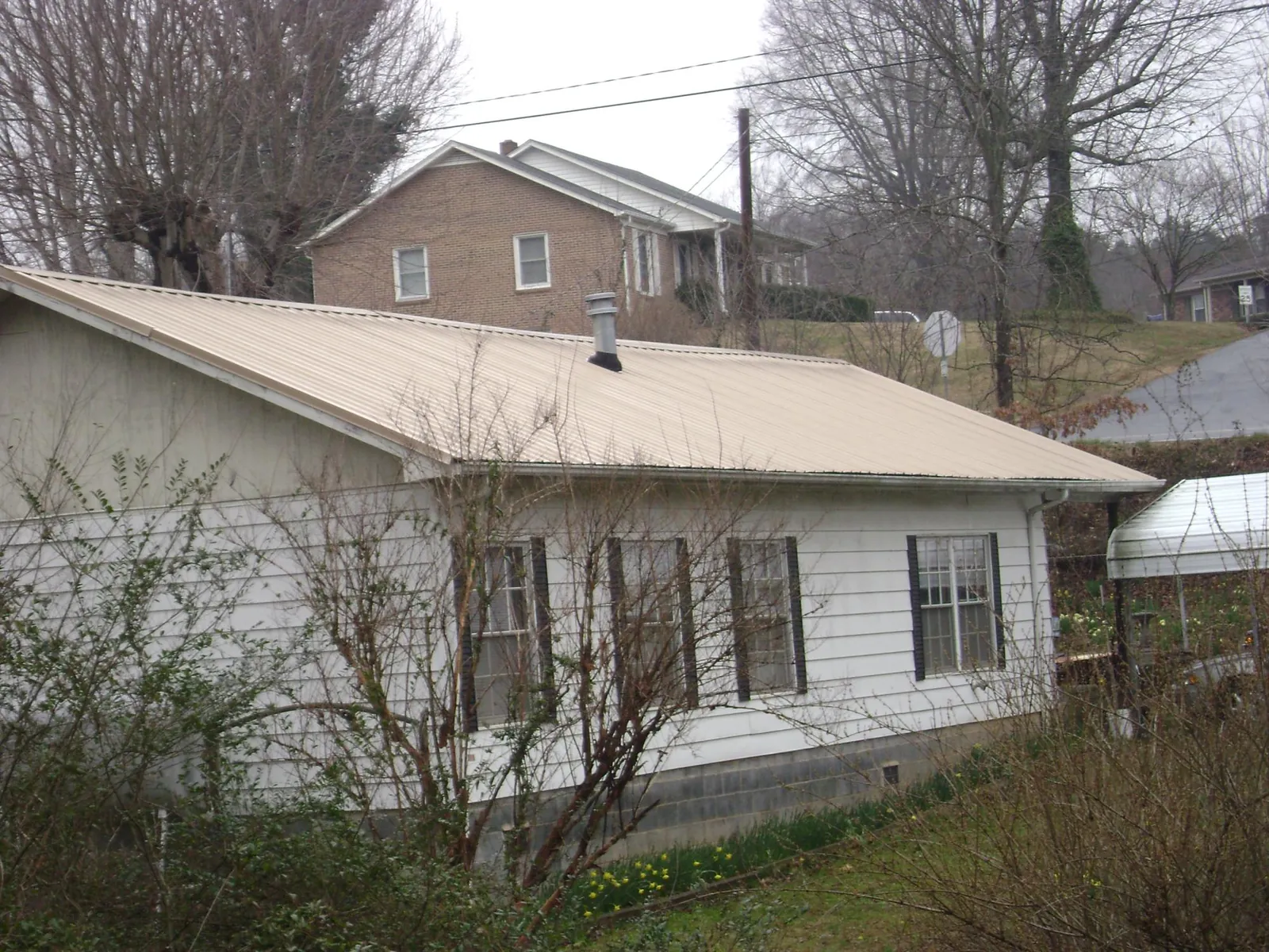 Tan metal roof on a white sided house set into a hillside — Commercial Roofing by Roofing Brothers in Willow Creek